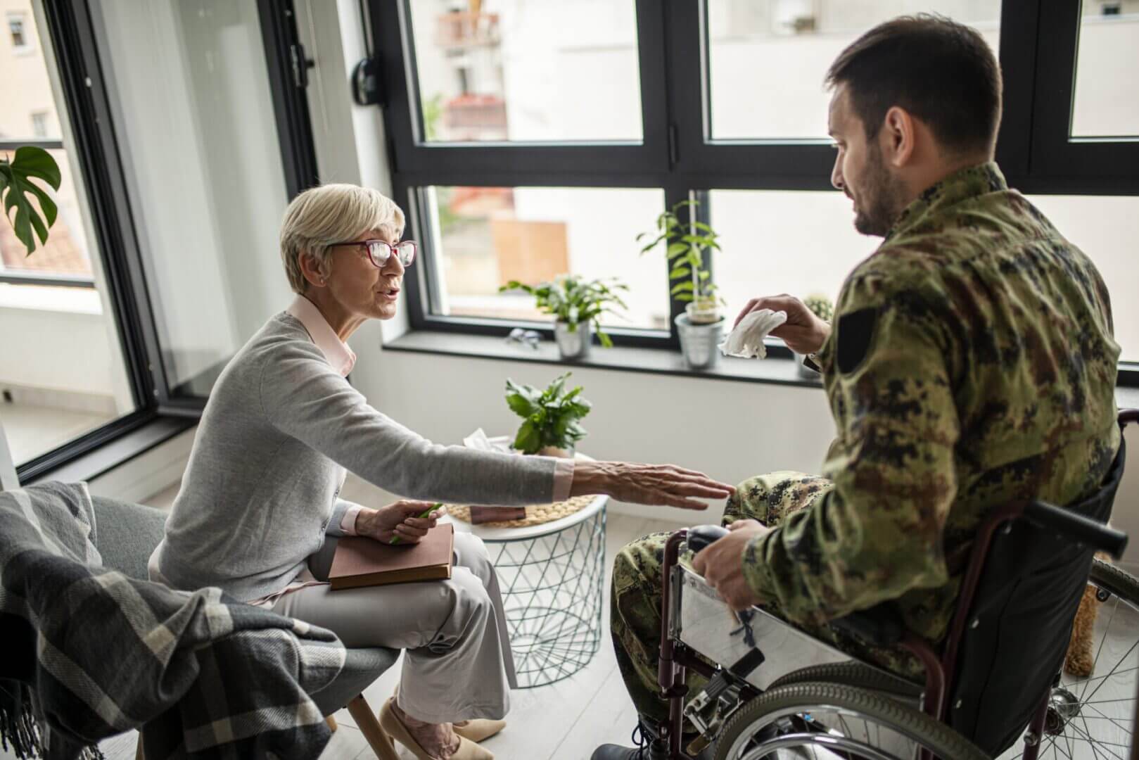 A military veteran in a wheelchair shaking hands with a woman indoors.